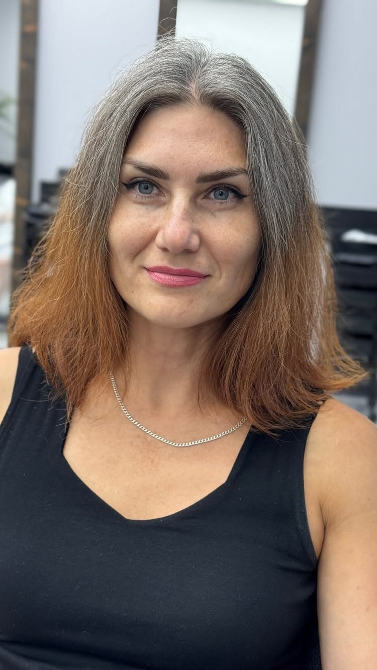 Woman with gray roots and long brown, copper-toned hair in a salon.