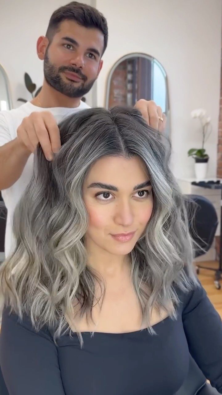 Woman with long wavy silver-gray hair and dark roots in a salon