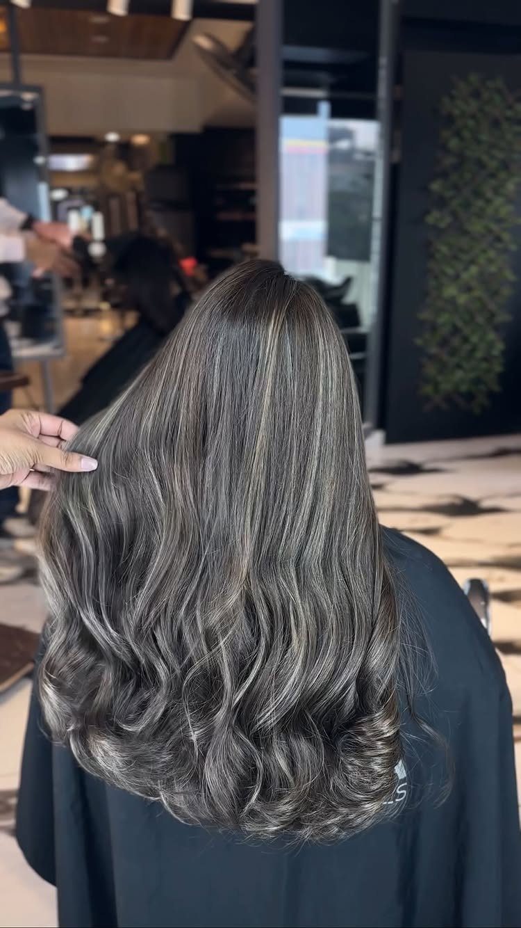 Wavy silver-gray and dark hair with blended lighter and darker strands in a salon