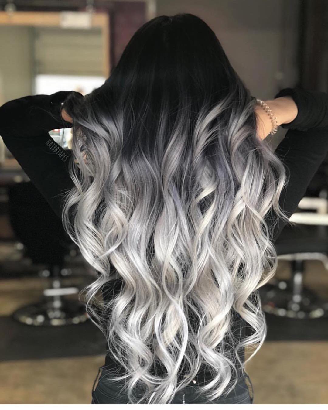 Long curled hair transitions from dark roots to icy silver-white ends