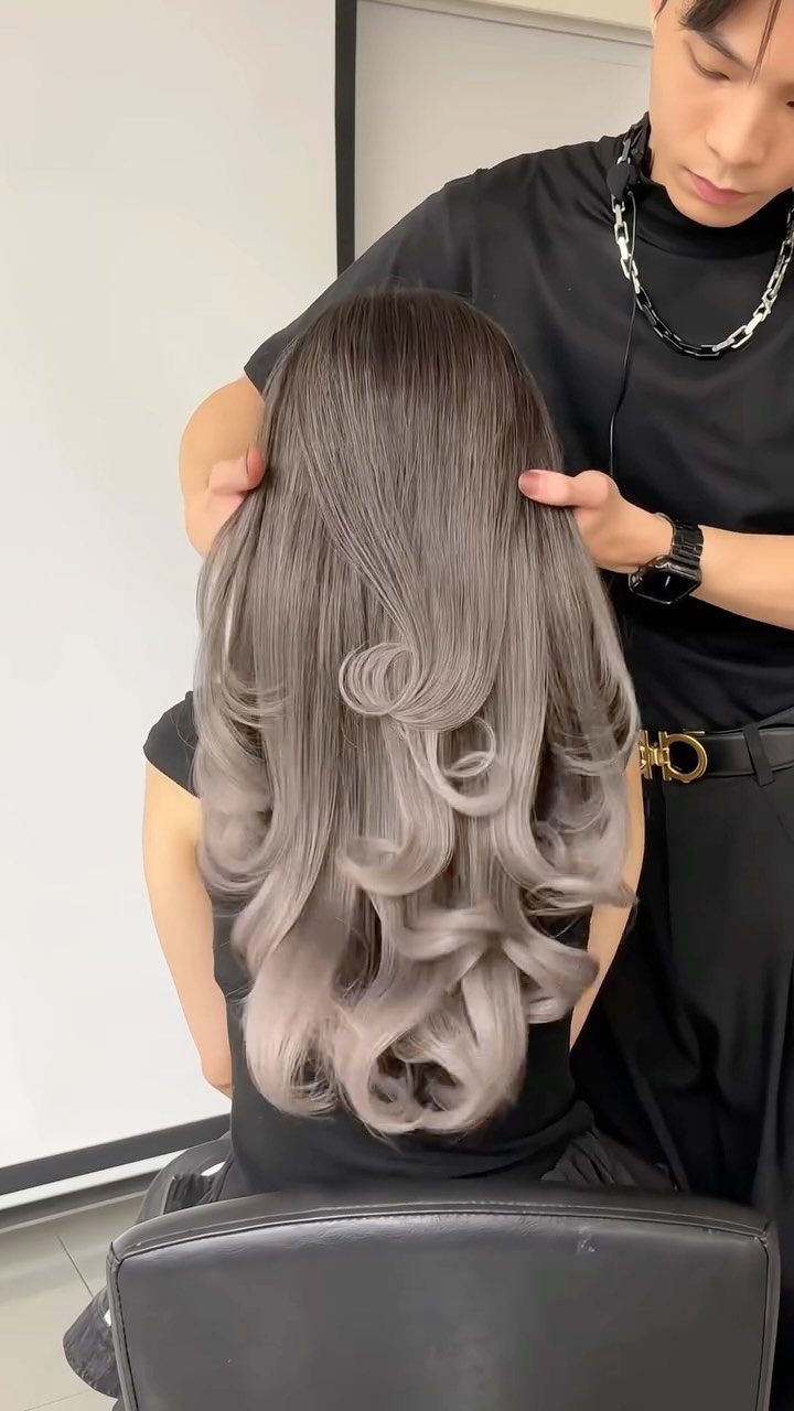 Long platinum-gray balayage curls with dark roots shown in a salon