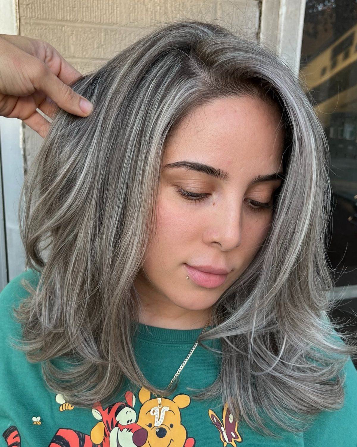 Woman with layered silver-gray highlights and dark roots, hair section held aside