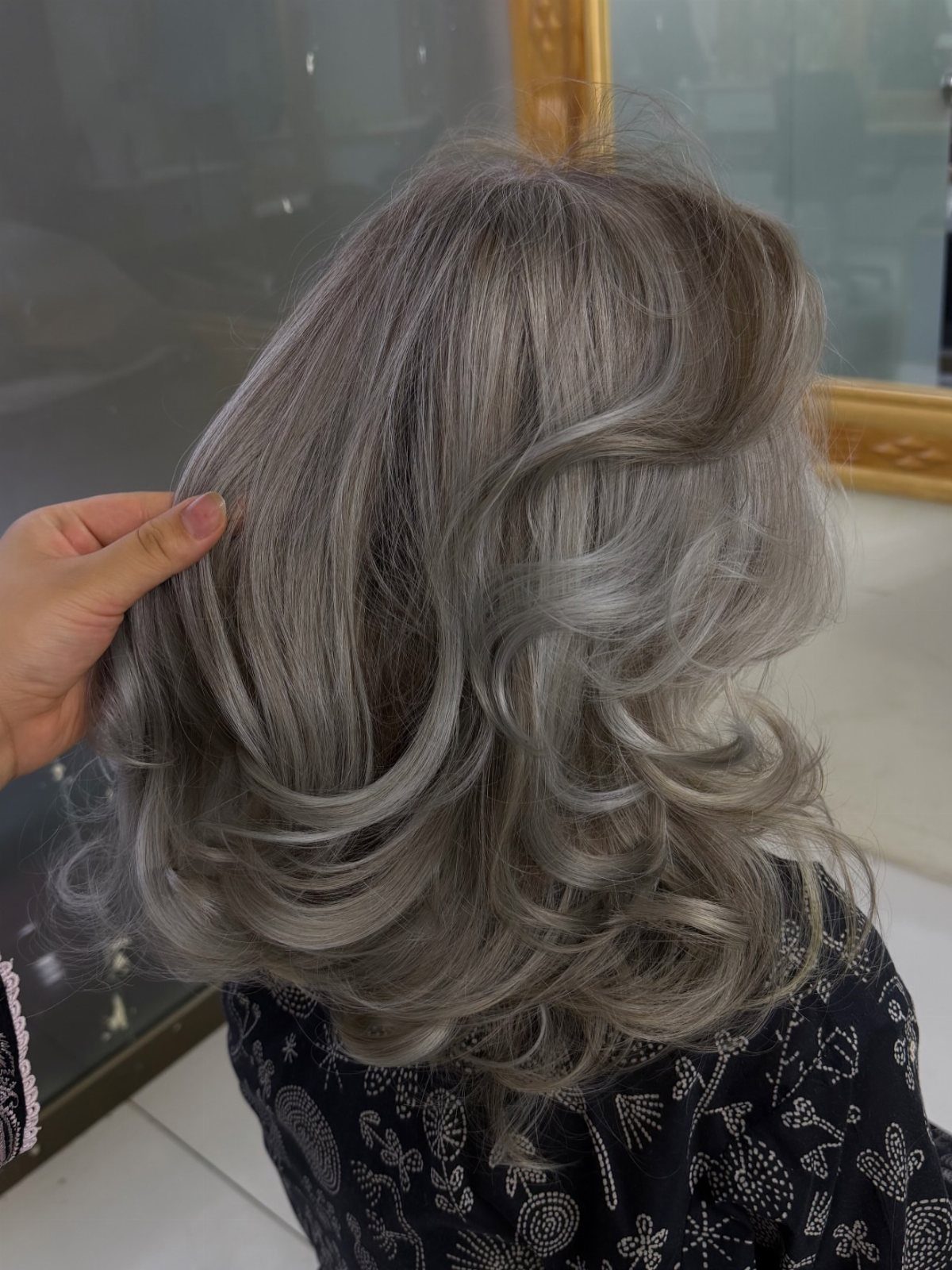 Long silver-gray curls with darker roots lifted by a hand