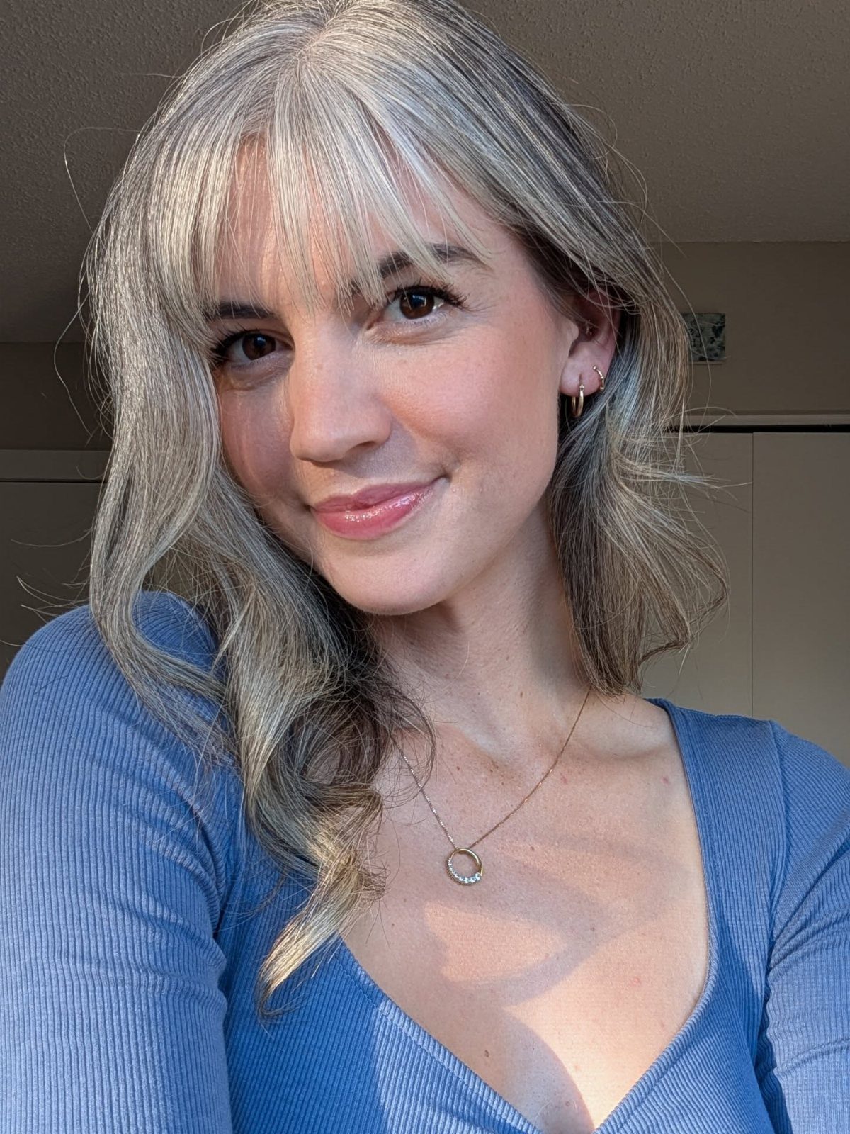 Woman with silver-grey bangs and loose face-framing strands wearing a blue top