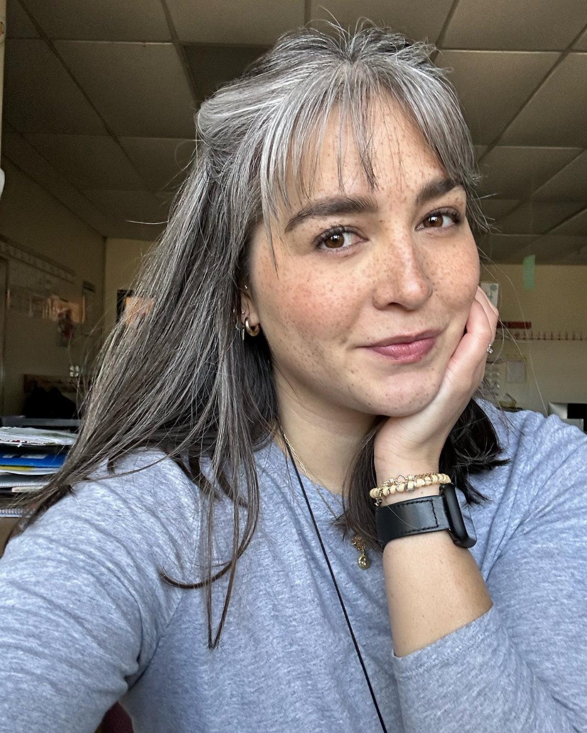 Woman with long salt-and-pepper hair and wispy bangs posing indoors