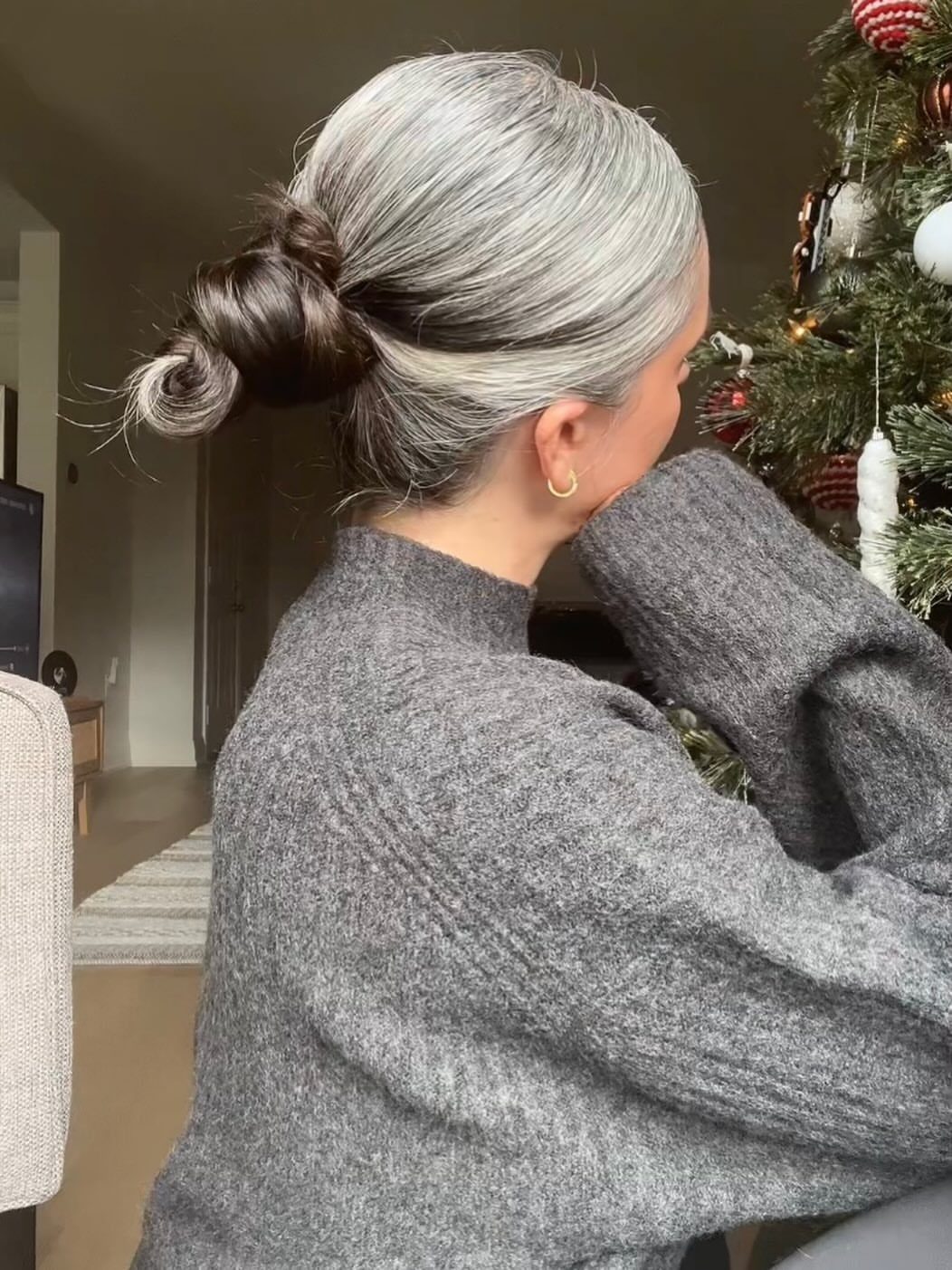 Silver-haired woman wears a loose low bun beside a decorated Christmas tree