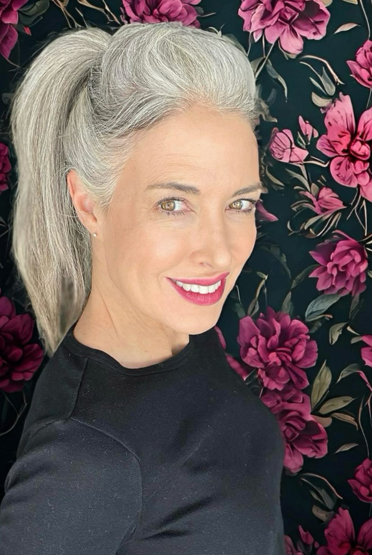 Woman with silver-grey hair styled in a high ponytail against floral wallpaper