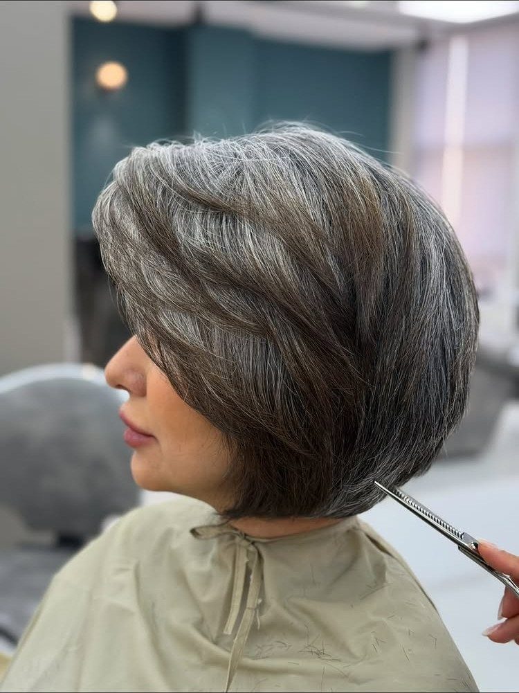 Silver-gray layered bob being trimmed by a stylist in a salon