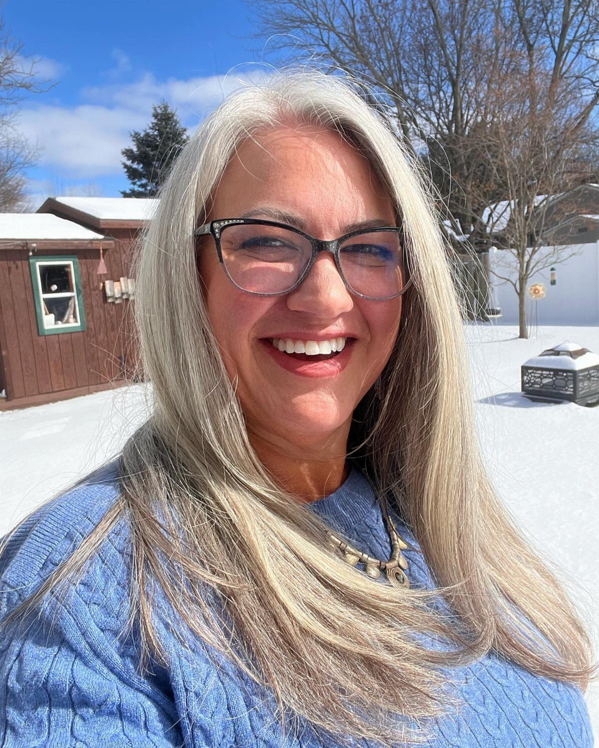 Woman with long straight silver-grey hair wearing glasses outdoors in snow
