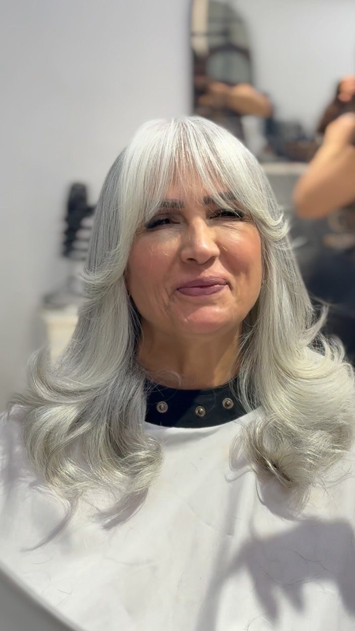 Woman with silver-grey feathered layers and straight bangs in a salon