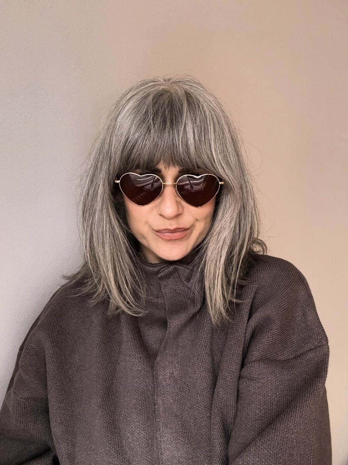 Woman with straight grey hair and full bangs wearing heart-shaped sunglasses