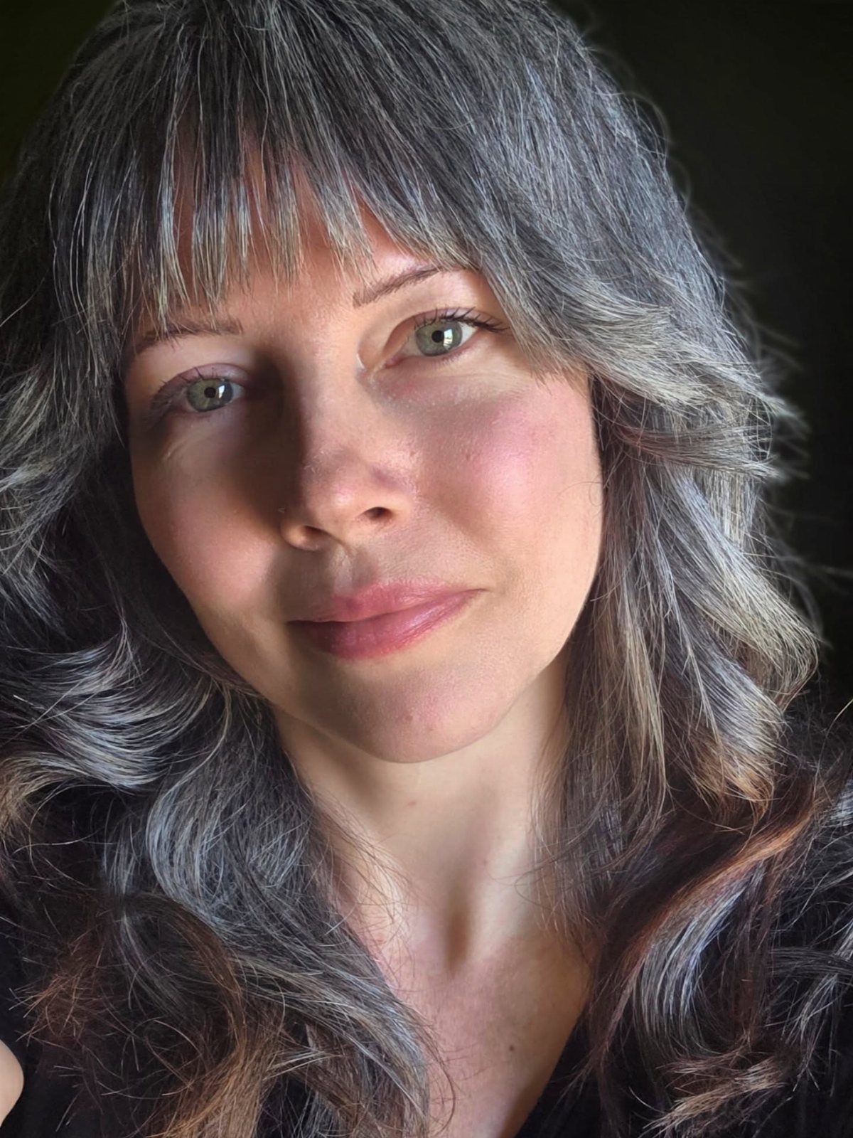 Woman with a layered fringe and long, wavy salt-and-pepper hair