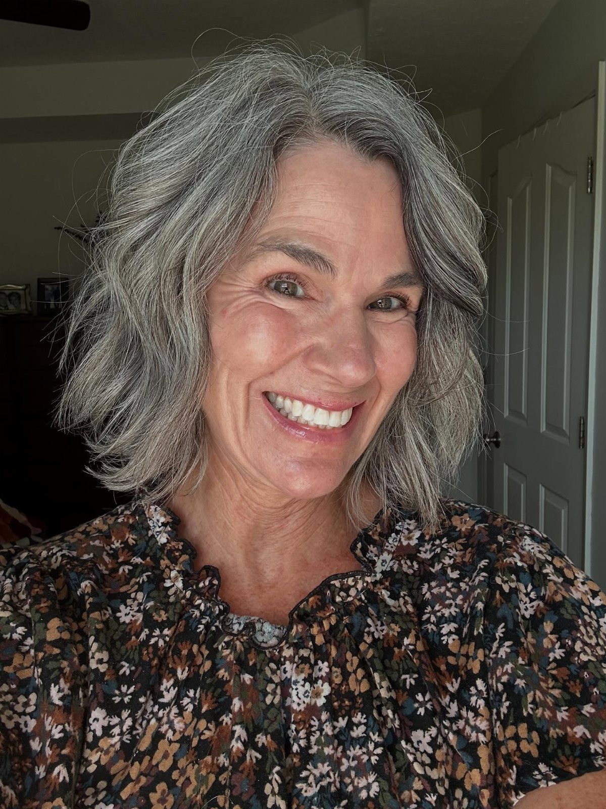 Woman smiling with shoulder-length silver-grey waves and a center part