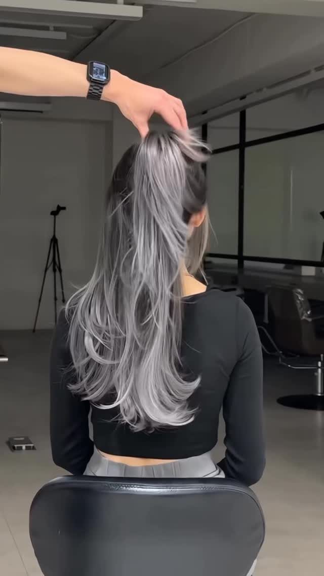 Long layered silver-gray hair with darker roots shown from behind in a salon
