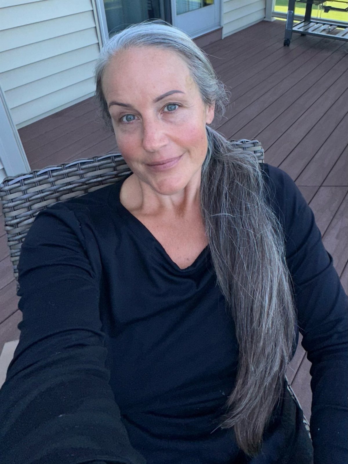 Woman displays long, straight silver-grey hair over one shoulder while seated outdoors