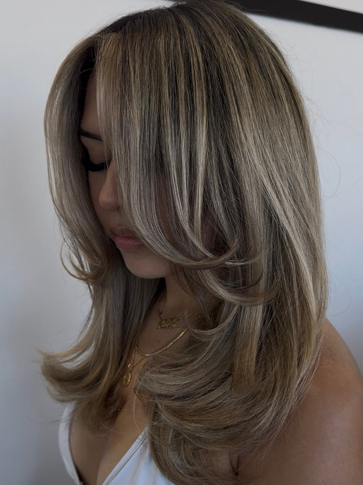 Woman displaying long layered beige-blonde hair with darker roots and pale highlights