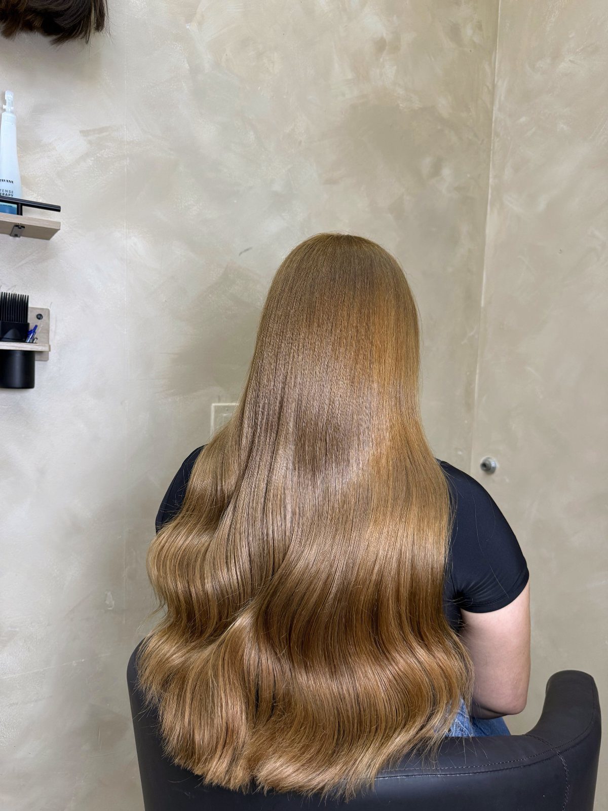 Long warm caramel-blonde waves displayed from behind in a salon chair
