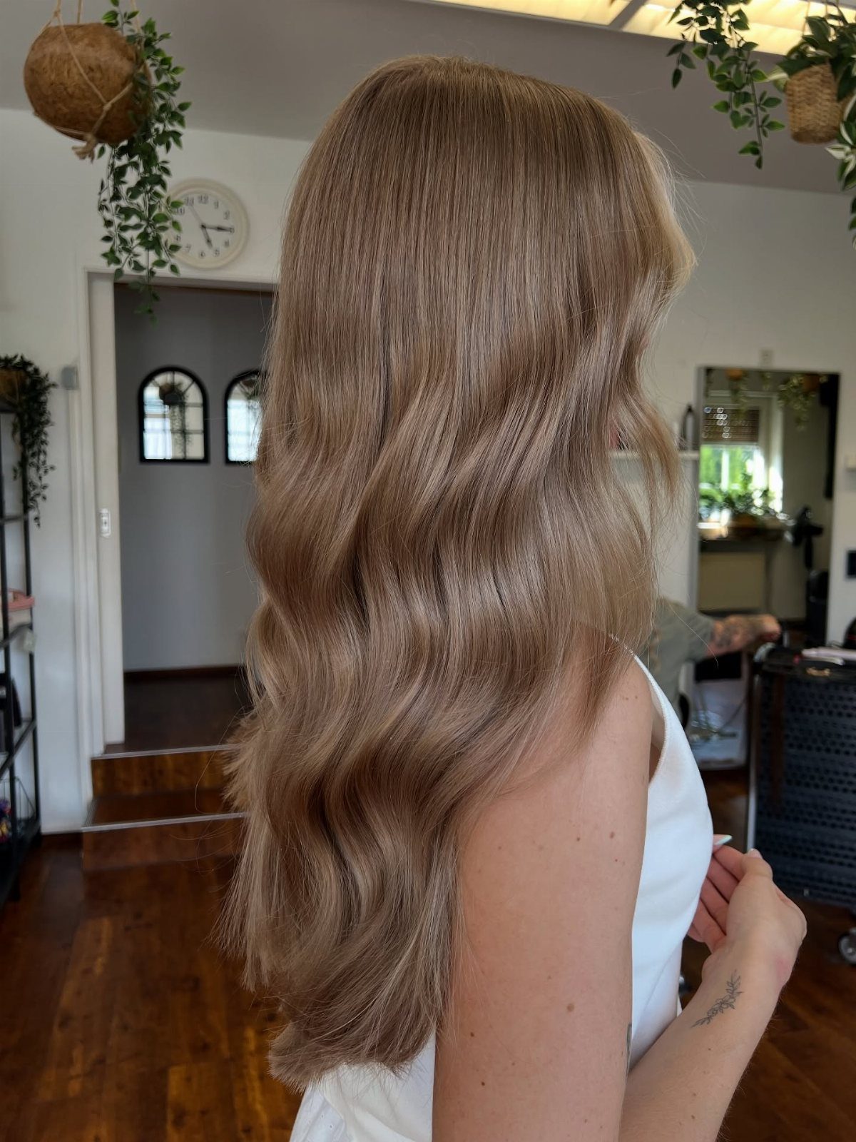 Long wavy dark blonde hair shown from behind in a bright salon