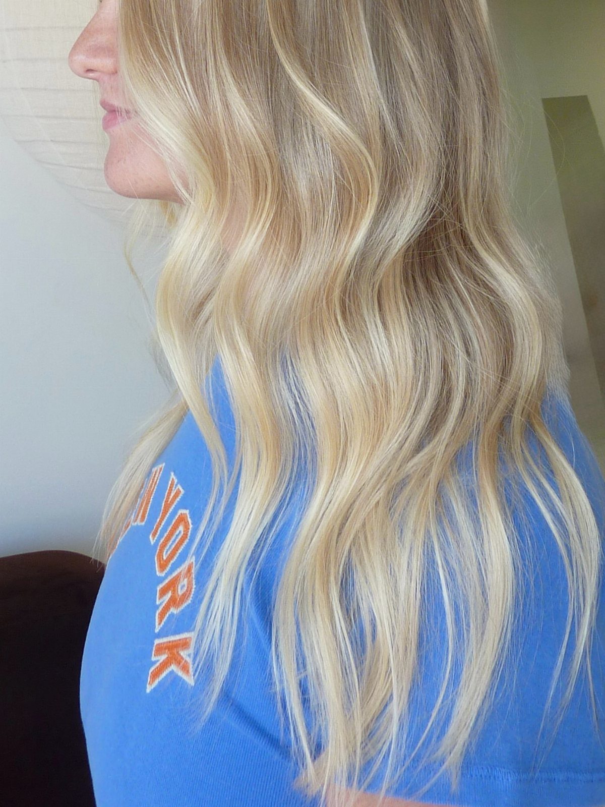 Long wavy light blond hair with beige and golden strands worn over a blue shirt