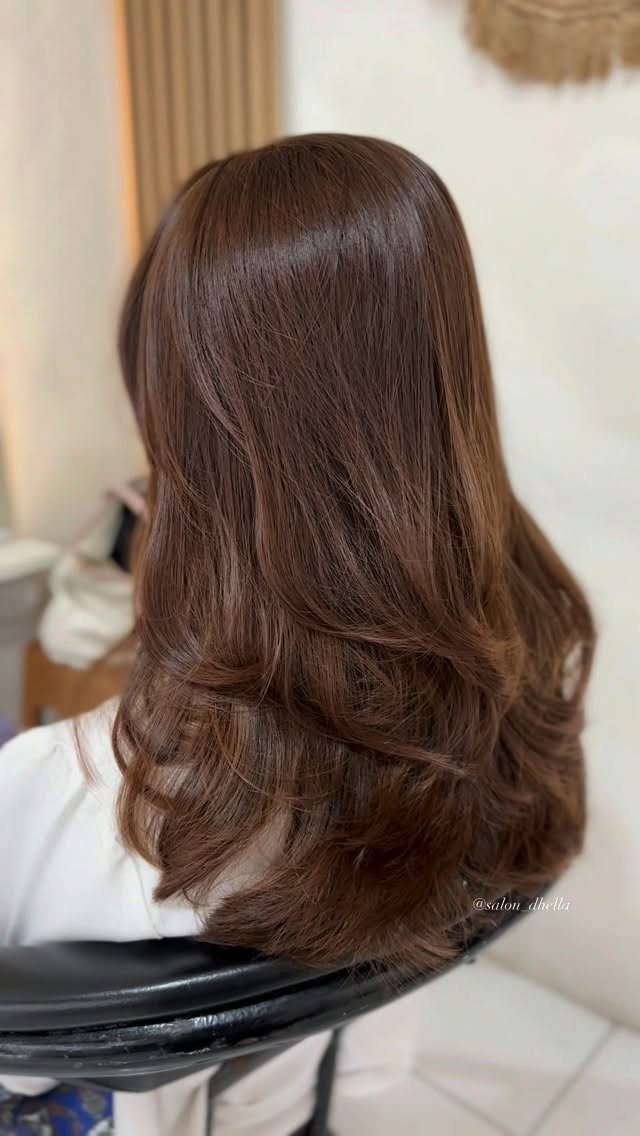Long warm golden-brown hair styled in glossy cascading waves over a salon chair