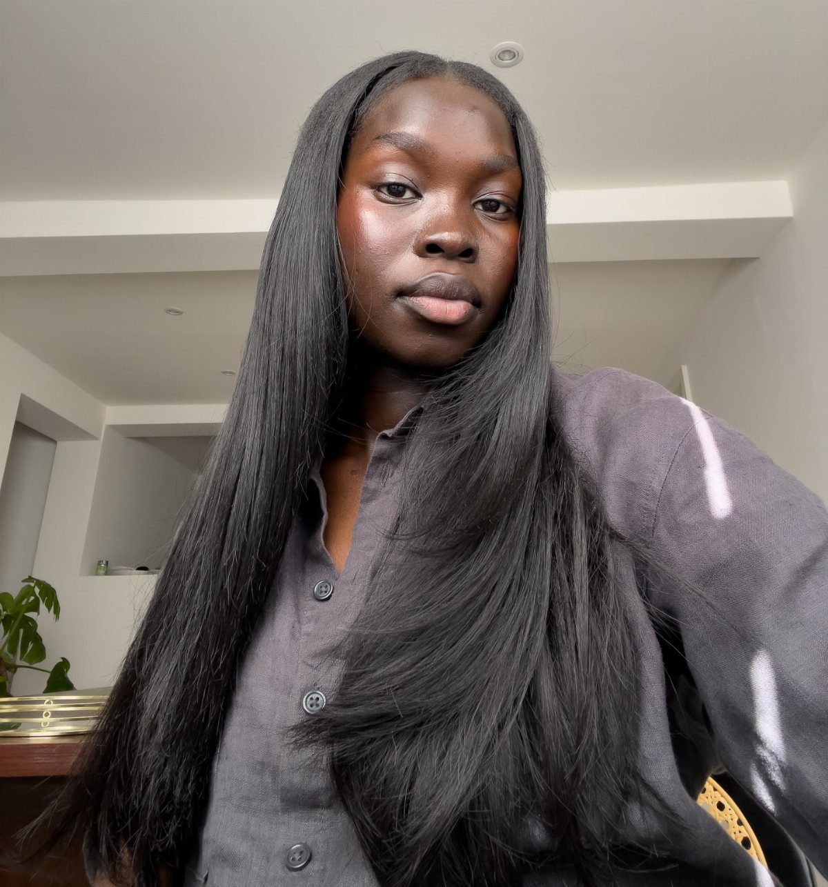 Woman with long, straight natural black hair posing indoors in a gray shirt