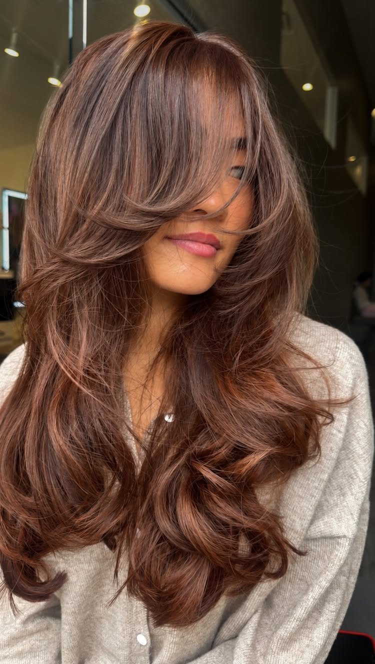 Long layered reddish-brown hair with sweeping bangs and glossy curled ends