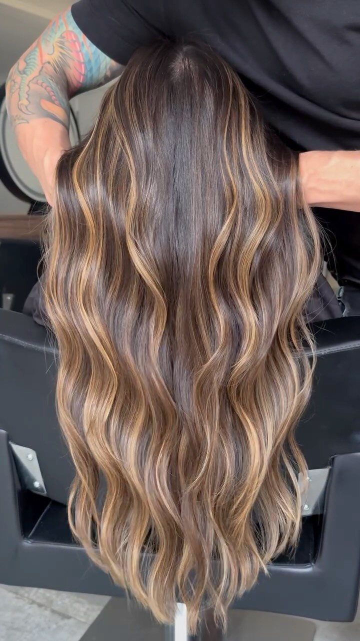 Wavy brown hair with hazelnut highlights cascading down a salon chair