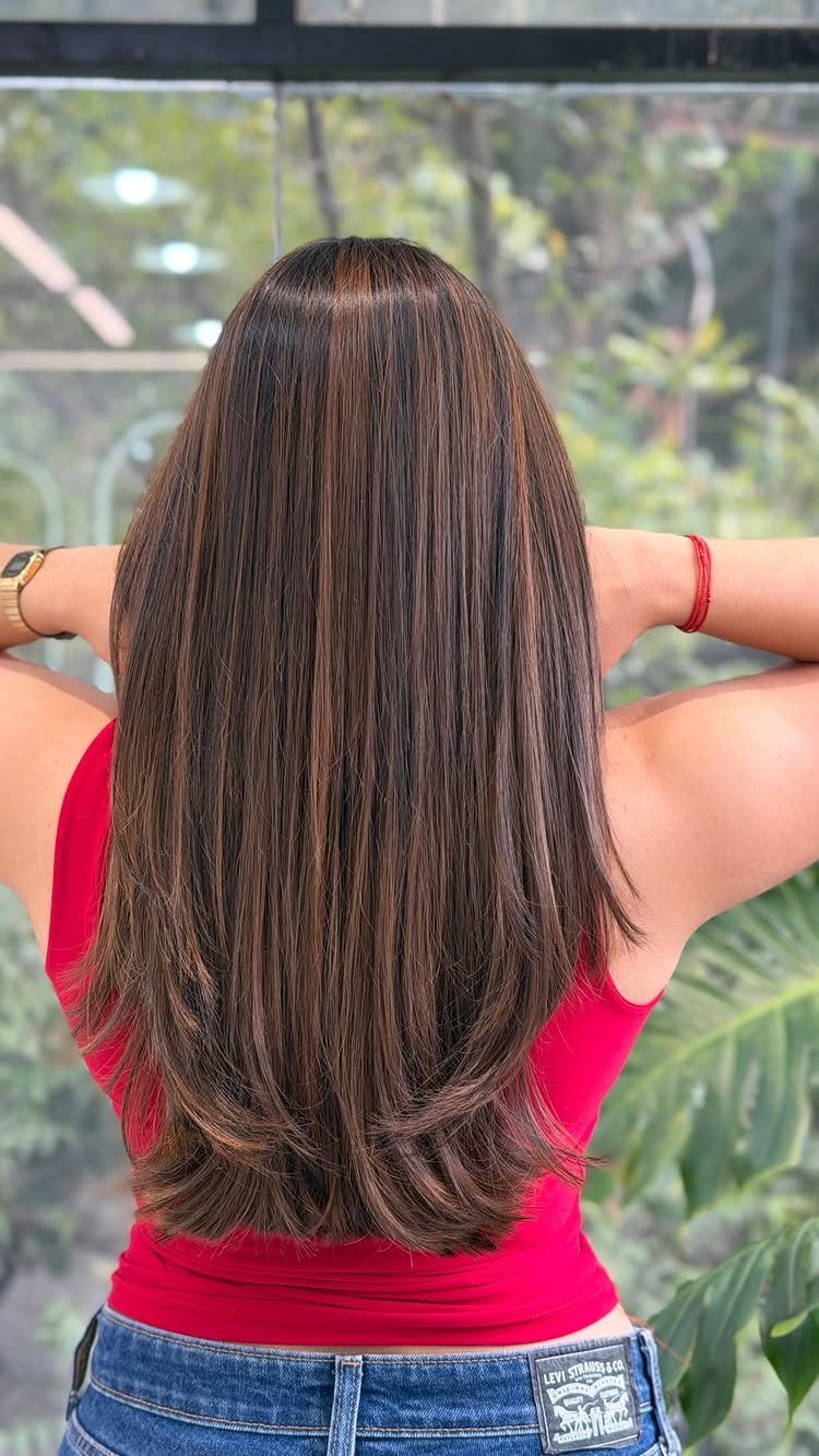 Long brown hair with warm caramel-toned strands falls over a bright pink top