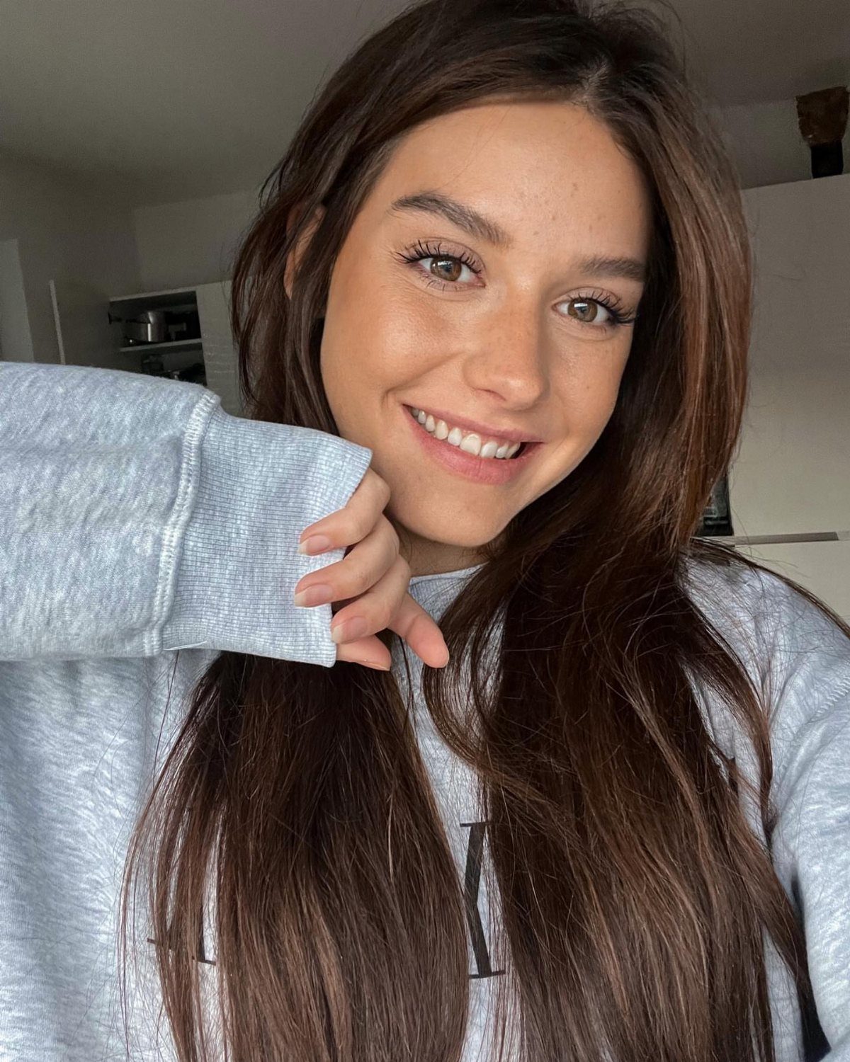 Woman smiling with long, rich chocolate brown hair and a gray sweatshirt