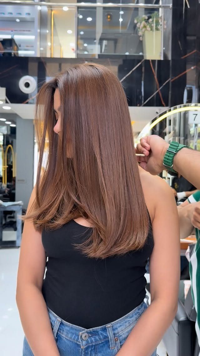Long cinnamon-brown layered hair shown from behind in a salon