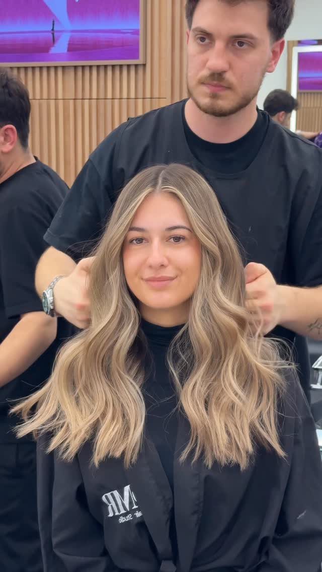 Woman with long, wavy sandy blonde hair seated in a salon chair
