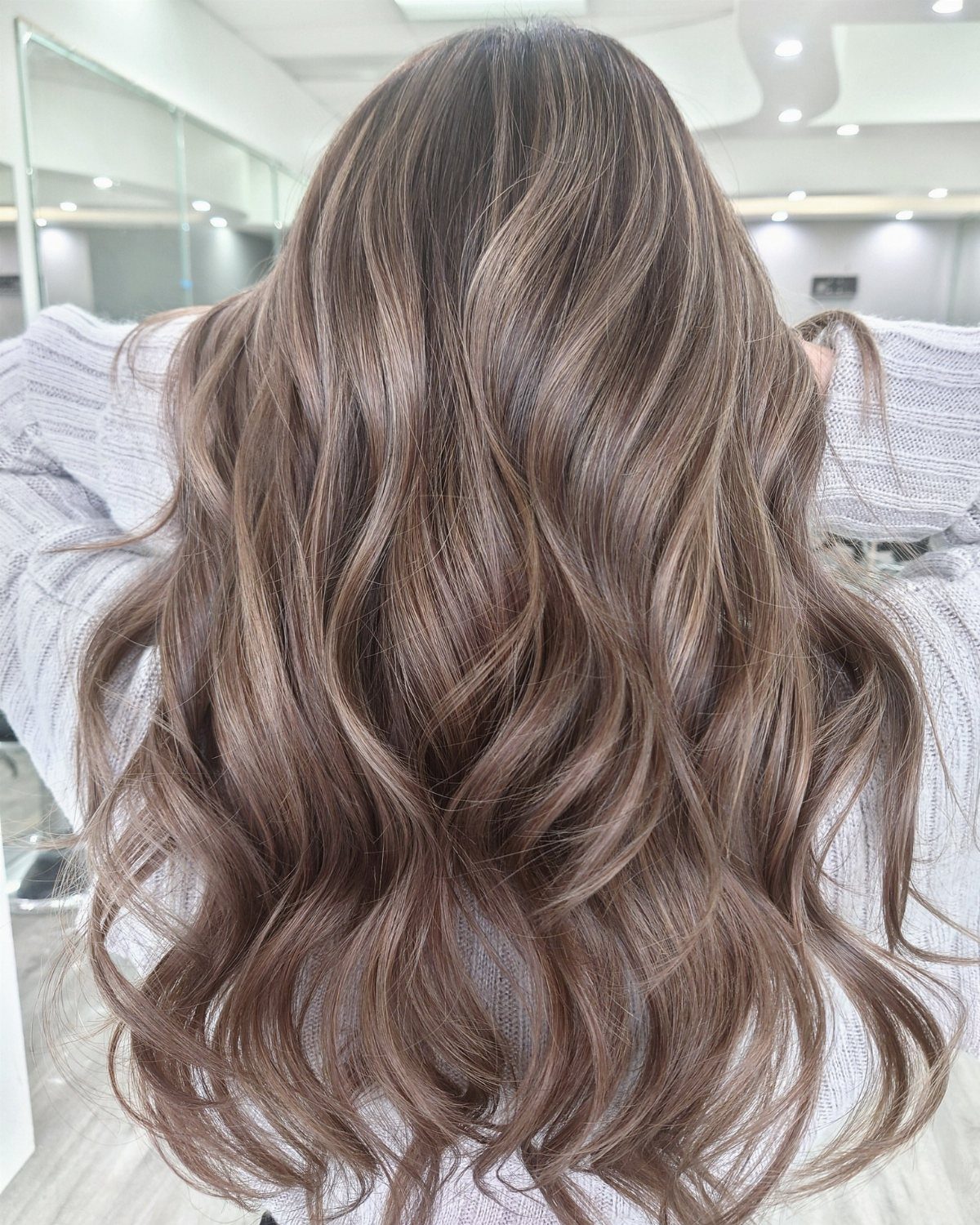 Long, wavy mushroom-brown hair with cool taupe highlights in a salon