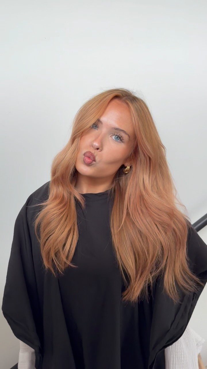 Woman with long, softly waved strawberry-blonde hair posing in a black salon cape