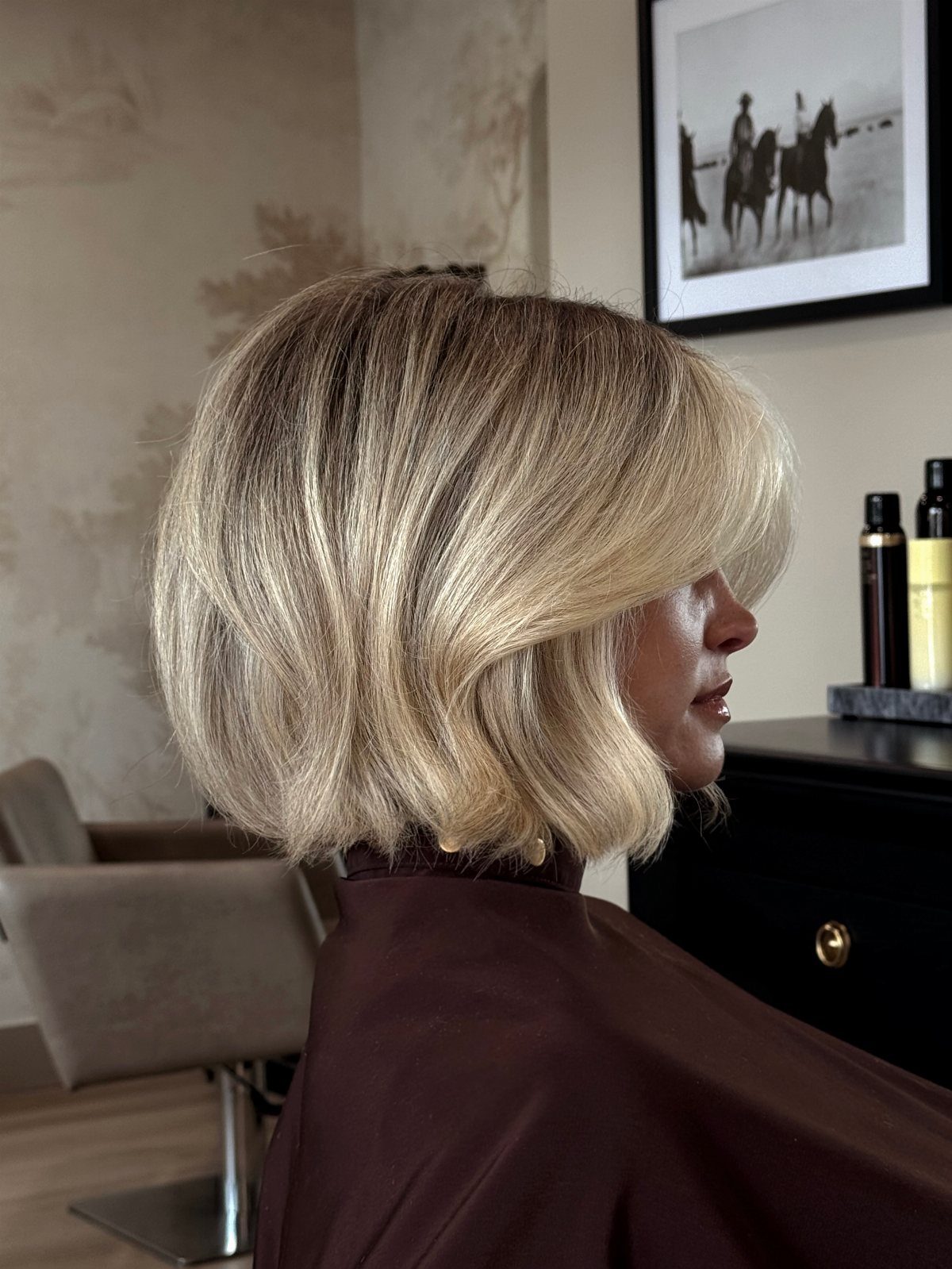 Short blonde bob with darker roots shown in profile in a salon