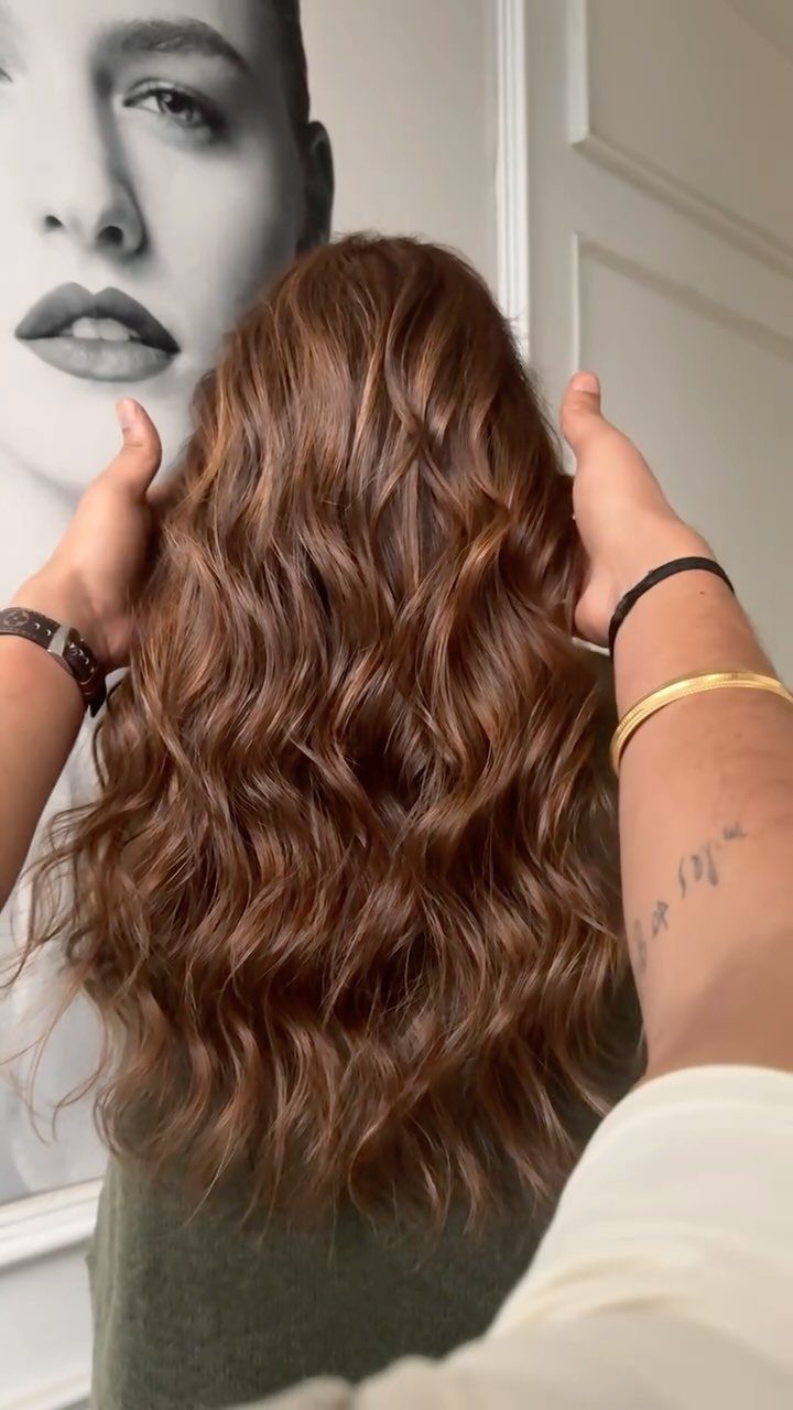 Wavy chestnut hair with warm balayage highlights held out by hands