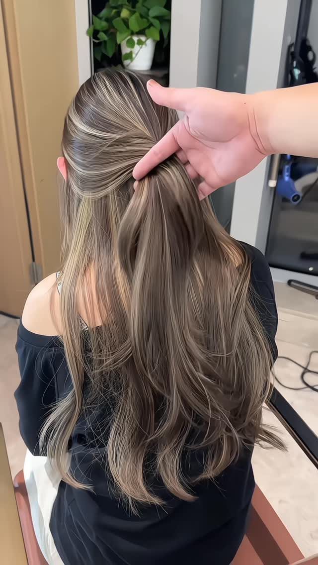 Fine blonde babylights blend through long, wavy brown hair in a salon