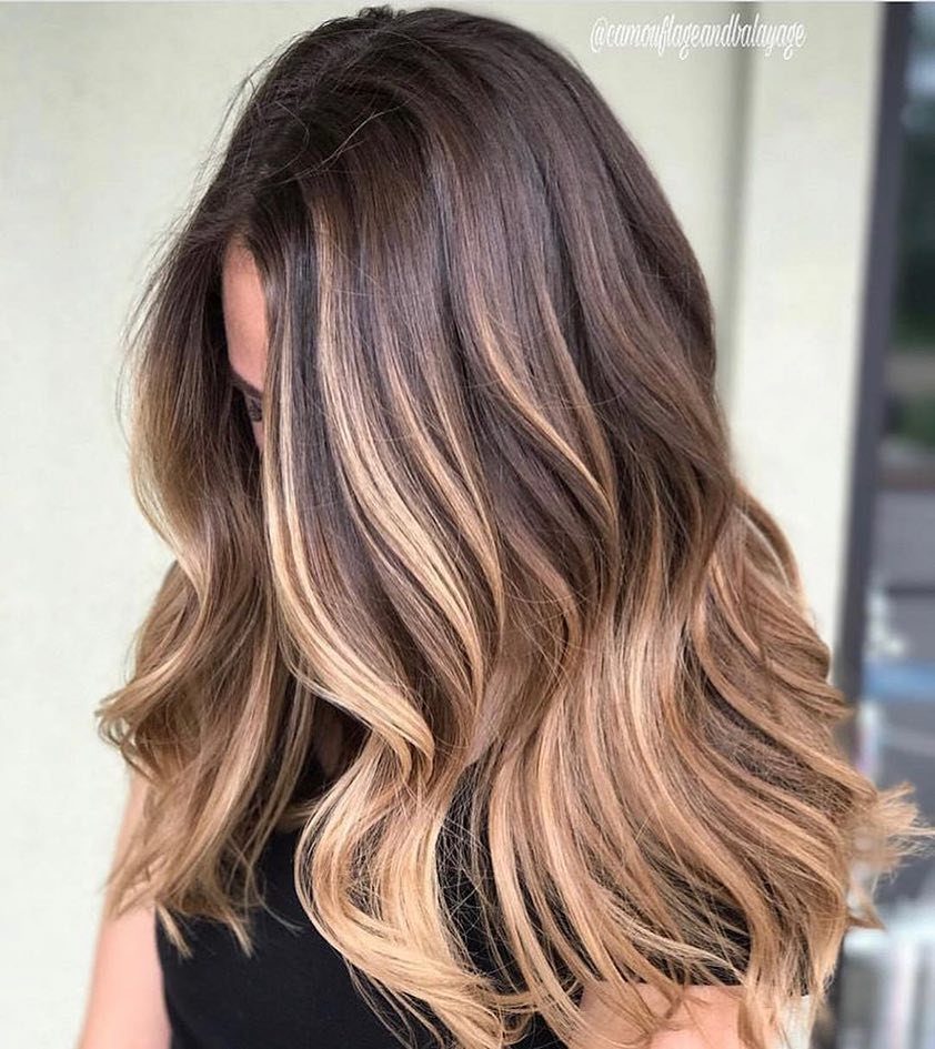 Wavy brunette hair with caramel highlights cascading over a black top