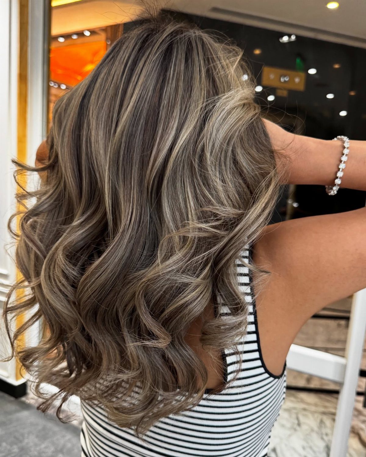 Cool ash highlights blend through curled dark brown hair in a salon