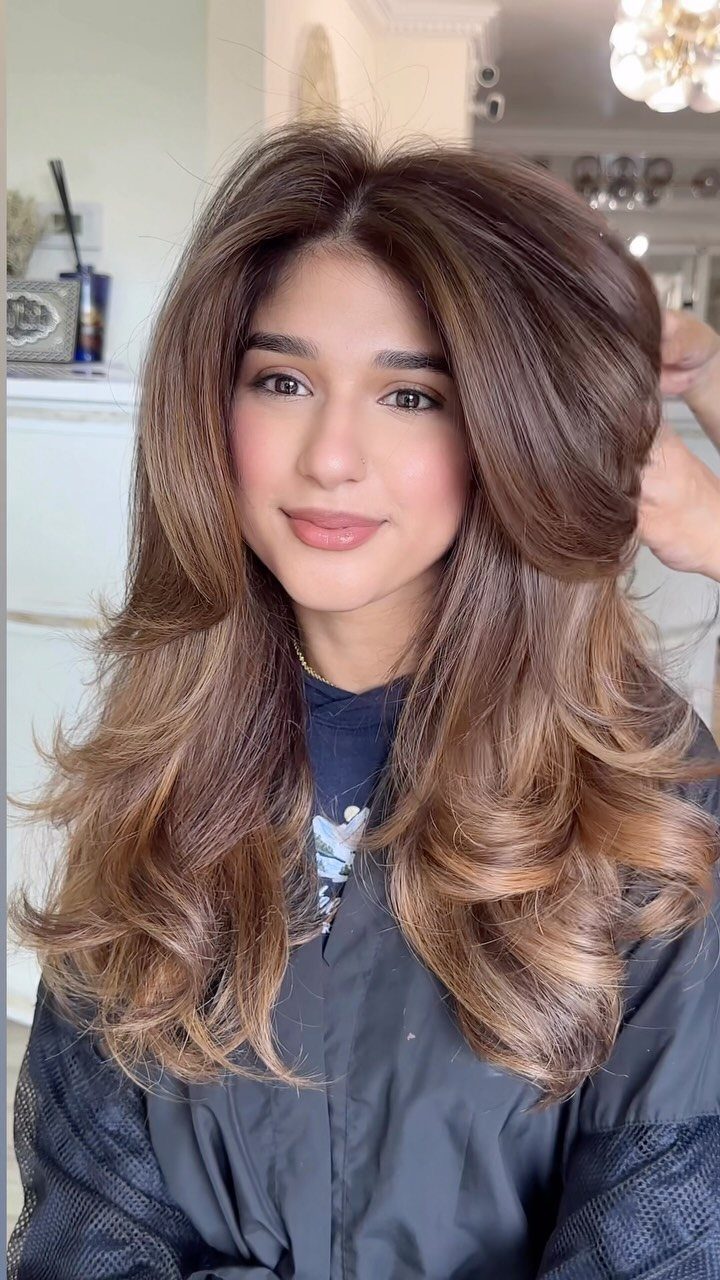 Woman showing long brown hair with golden caramel balayage highlights in a salon