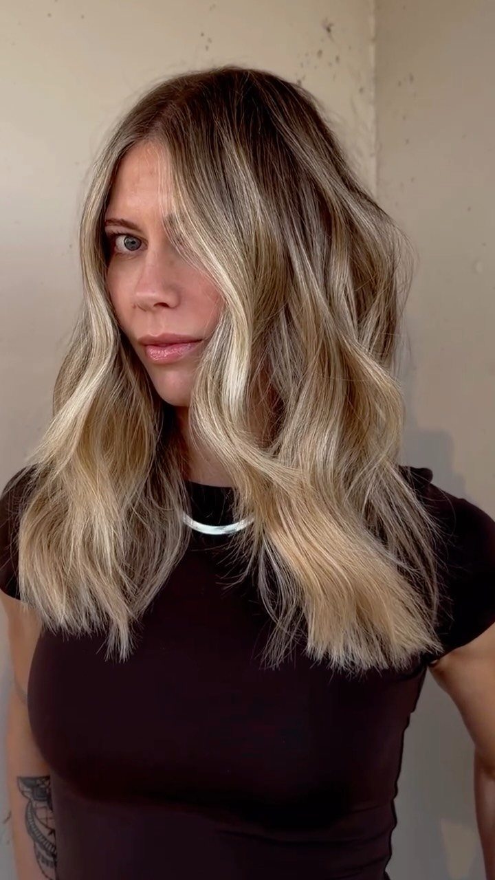 Woman with long wavy blonde hair featuring warm golden highlights and darker roots