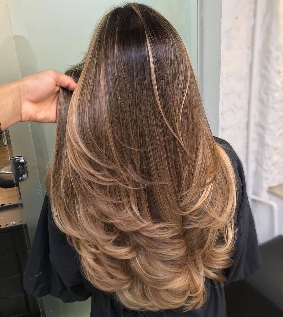 Layered brown hair with honey-blonde highlights and softly curled ends in a salon