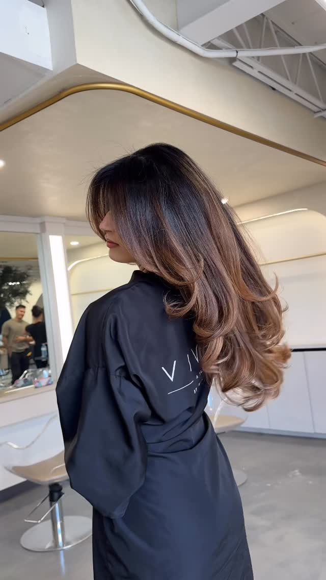 Long brunette hair with warm caramel tones in a bright salon