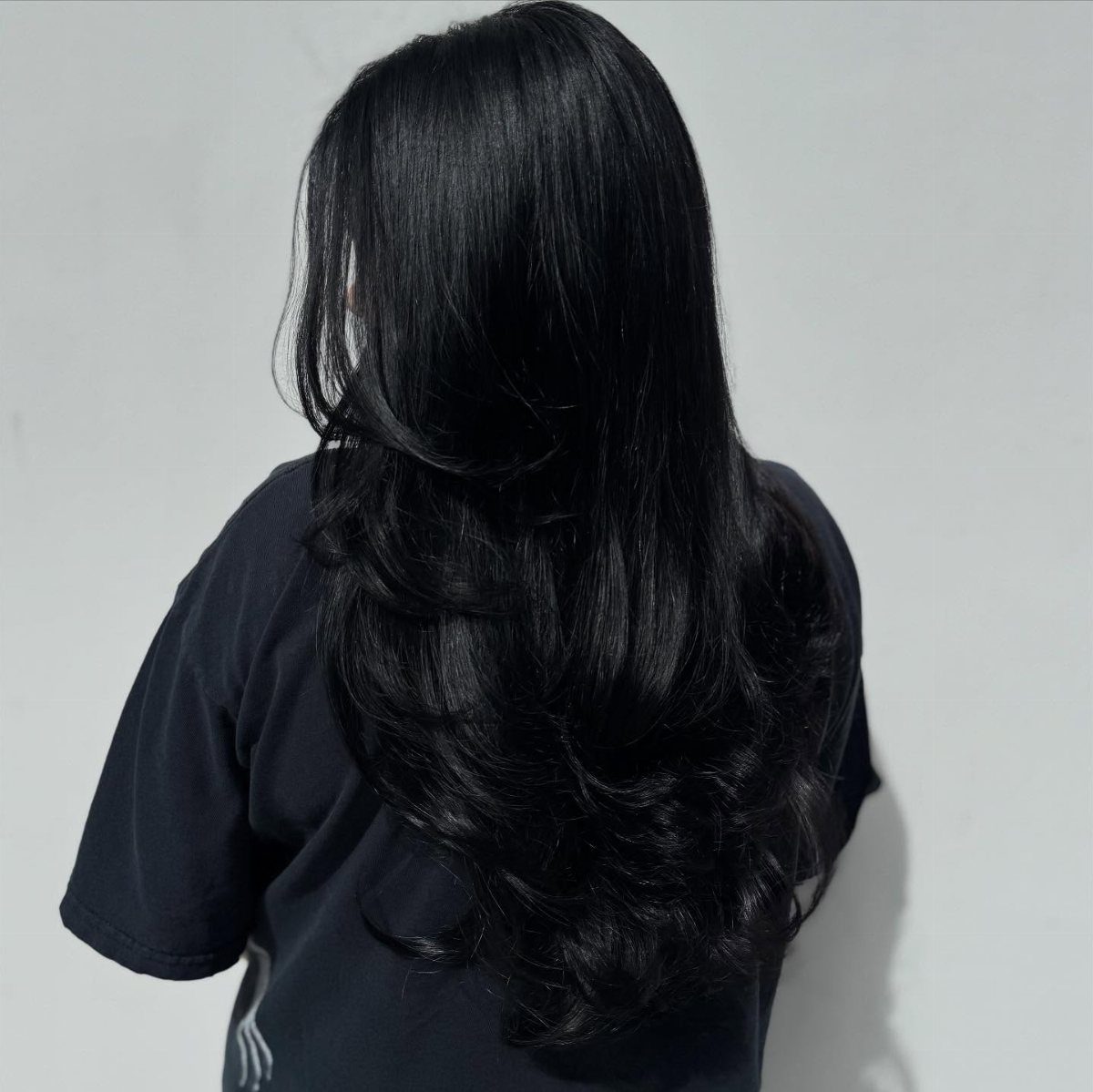 Long glossy jet-black hair falls in loose curls over a black shirt.