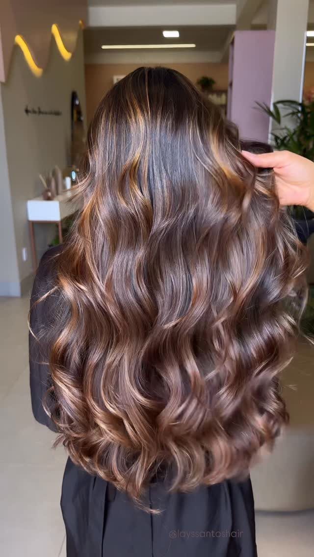 Long curled brunette hair with soft light-brown notes in a salon