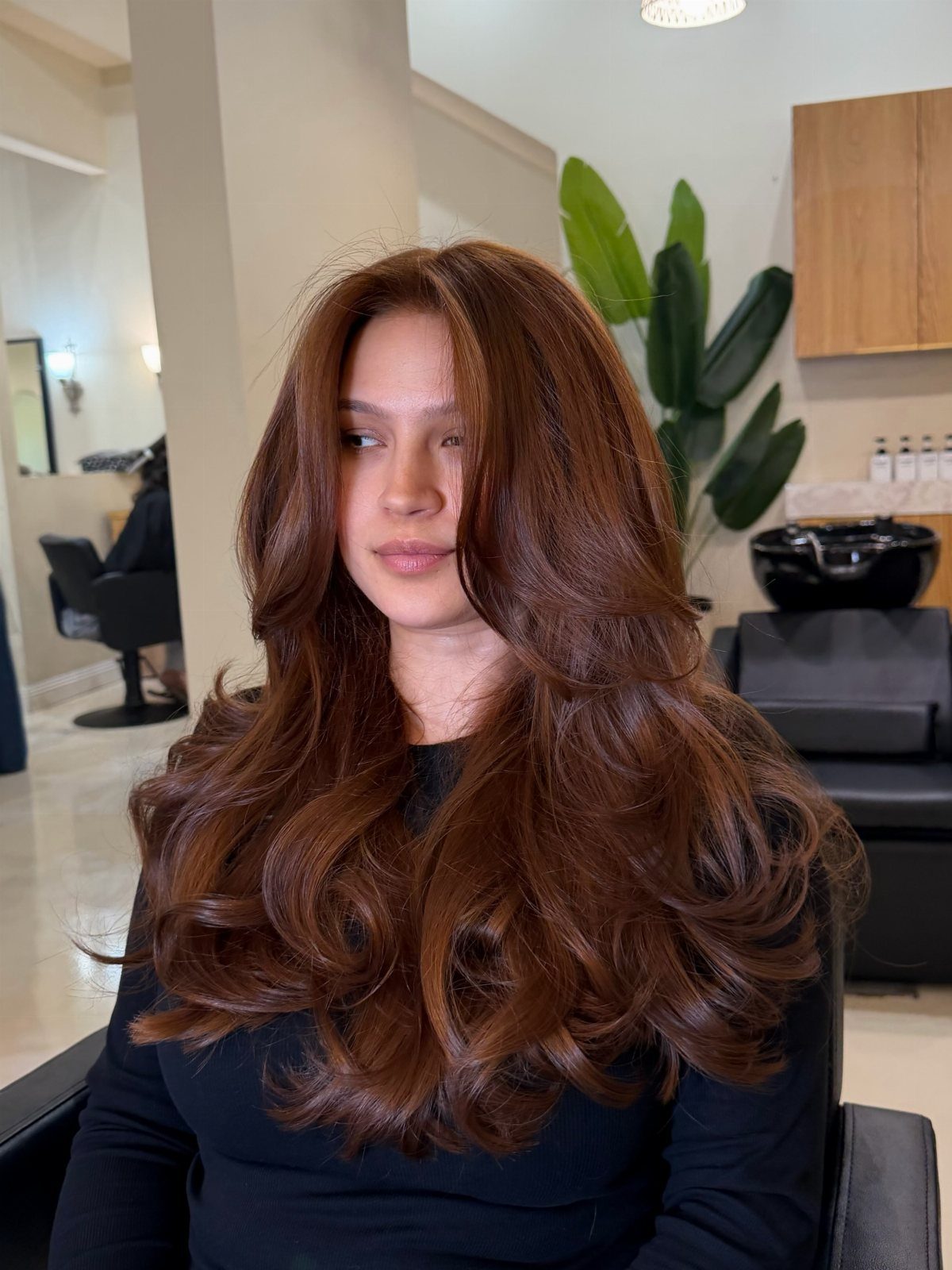 Woman with long, voluminous reddish-brown waves in a salon chair