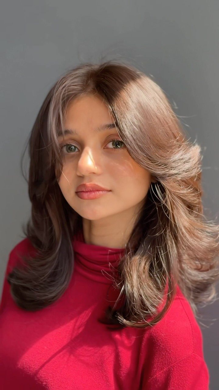 Woman with layered light brown hair and curtain bangs wearing a red top