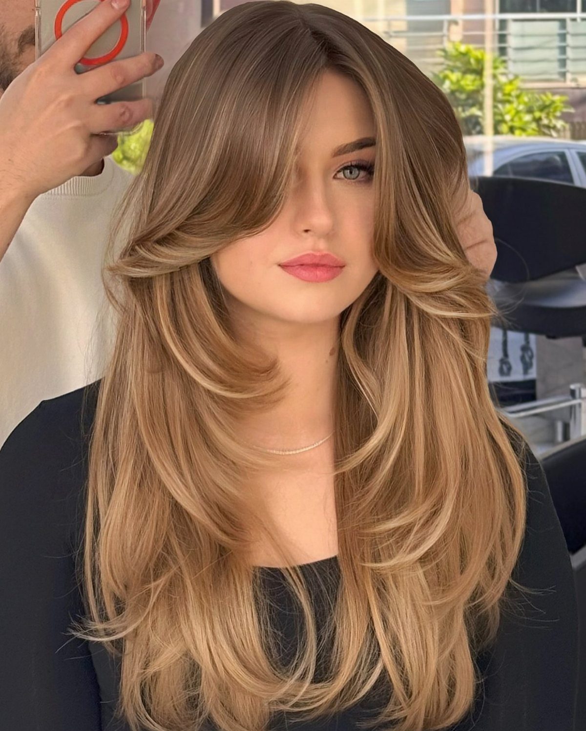 Woman with long, layered golden light brown hair and curled ends in a salon
