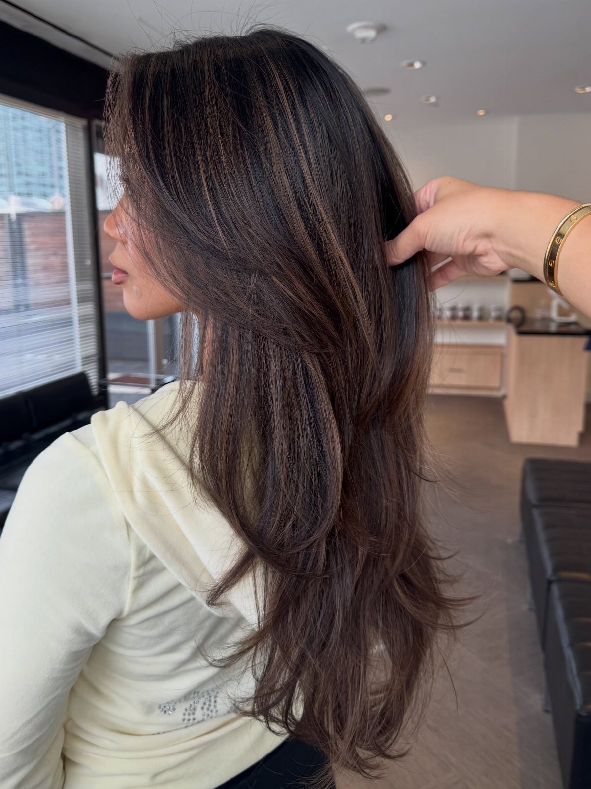 Long dark brown hair with subtle lighter brown strands lifted in a salon chair