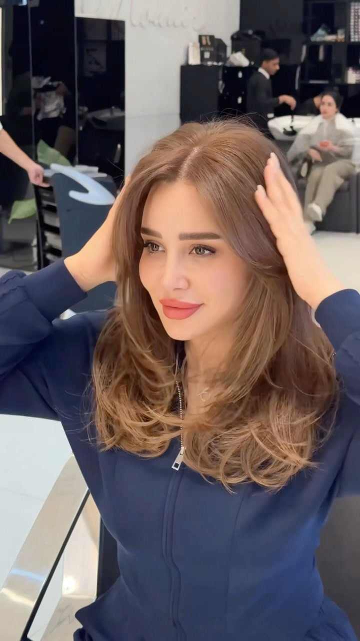 Woman with long, softly waved light brown hair in a salon chair