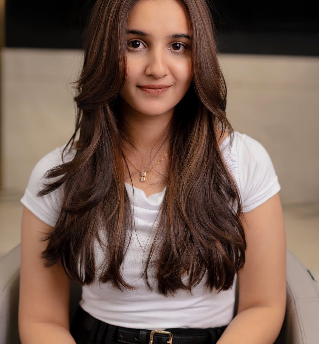 Woman with long, layered brown hair and loose waves wearing a white shirt